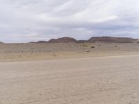 an empty desert with dirt and sand hills behind it and clouds overhead over the mountains