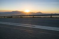 the road is empty and the sun rises behind some mountains along the highway side, with one half in the distance