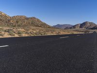 a person on a motorbike driving down an empty street with desert mountains and mountains in the distance