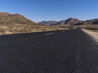 a person on a motorbike driving down an empty street with desert mountains and mountains in the distance