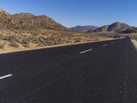 a person on a motorbike driving down an empty street with desert mountains and mountains in the distance