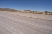 a long straight road runs through a desert plain, near a large, mountain in the distance