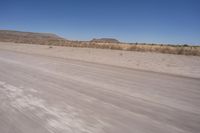 a long straight road runs through a desert plain, near a large, mountain in the distance