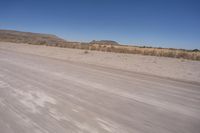 a long straight road runs through a desert plain, near a large, mountain in the distance