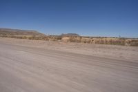 a long straight road runs through a desert plain, near a large, mountain in the distance