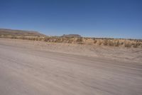 a long straight road runs through a desert plain, near a large, mountain in the distance