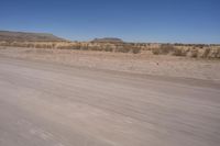 a long straight road runs through a desert plain, near a large, mountain in the distance