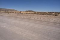 a long straight road runs through a desert plain, near a large, mountain in the distance