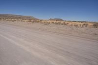 a long straight road runs through a desert plain, near a large, mountain in the distance