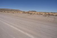 a long straight road runs through a desert plain, near a large, mountain in the distance