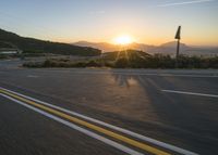 the sun sets over a mountain near a highway with a motorcycle on it with a yellow line