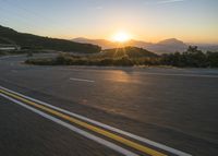 the sun sets over a mountain near a highway with a motorcycle on it with a yellow line