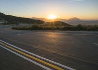 the sun sets over a mountain near a highway with a motorcycle on it with a yellow line