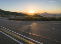 the sun sets over a mountain near a highway with a motorcycle on it with a yellow line