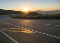 the sun sets over a mountain near a highway with a motorcycle on it with a yellow line