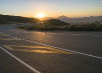 the sun sets over a mountain near a highway with a motorcycle on it with a yellow line