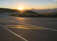 the sun sets over a mountain near a highway with a motorcycle on it with a yellow line