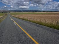 a lone road in an open field with trees on either side of it and mountains in the background