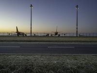 three jet planes sitting on the runway next to the grass at sunset from inside an airport