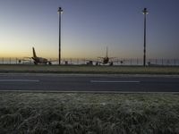 three jet planes sitting on the runway next to the grass at sunset from inside an airport