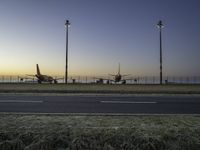 three jet planes sitting on the runway next to the grass at sunset from inside an airport