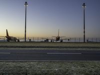 three jet planes sitting on the runway next to the grass at sunset from inside an airport