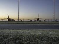 three jet planes sitting on the runway next to the grass at sunset from inside an airport