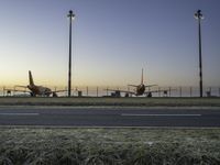 three jet planes sitting on the runway next to the grass at sunset from inside an airport