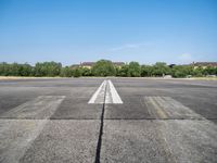 airplane line on a paved airport runway on a clear day with trees in the background