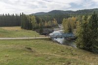 a blue metal bridge over a river on a green hillside with forest and trees on either side