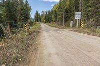 a dirt road surrounded by trees with caution signs on the side of the road next to it