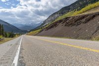 the road is lined with mountains and pines, with the road passing by it is very windy