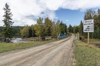 dirt road with train crossing over a bridge to a small creek below, trees and mountains