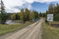 dirt road with train crossing over a bridge to a small creek below, trees and mountains