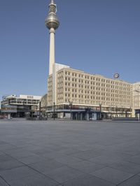 the television tower stands tall behind other buildings, in the city square of a large city