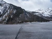 a mountain road with mountains and trees in the background in wintertime under cloudy skies