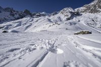 a snowboarder going down the side of a slope, toward some large snow mountains