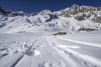 a snowboarder going down the side of a slope, toward some large snow mountains