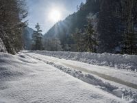 the road with many tracks made in the snow on it has the sun shining through the trees