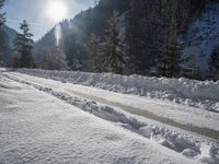 the road with many tracks made in the snow on it has the sun shining through the trees