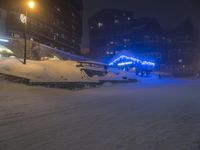 some people on skis in the snow and buildings in the background, by the street lights