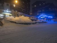 some people on skis in the snow and buildings in the background, by the street lights