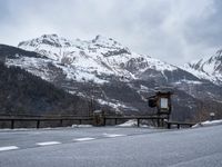 a stop light on the side of the road next to a snowy hill range with a fence in front of it