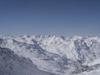 snow covered mountain range and ski slope with a skier looking out to the mountain valley