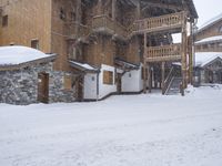 the building is wooden and has snow on it in winter time is surrounded by stone and concrete, in front of the sidewalk are small cottages with stairs