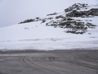 the road is made of asphalt with snow piled up to the side of it and mountains are in the background