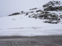 the road is made of asphalt with snow piled up to the side of it and mountains are in the background