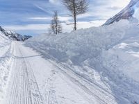 a snowy road going through the mountains, and with tracks in it, in front of a tree with three snow skis