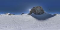 snow covered ground with large rocks in distance under bright sky with sun glaring on snow