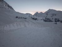 a mountain is shown at dusk, with a ski slope and a line of trees visible